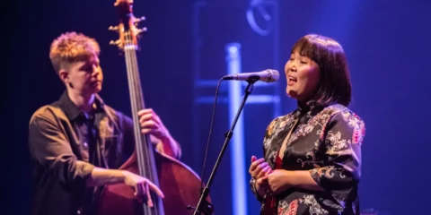 Chanteuse sur scène avec contrebassiste sous éclairage bleu.