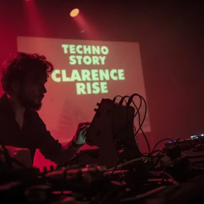 DJ Clarence Rise mixant dans un club sous lumière rouge.